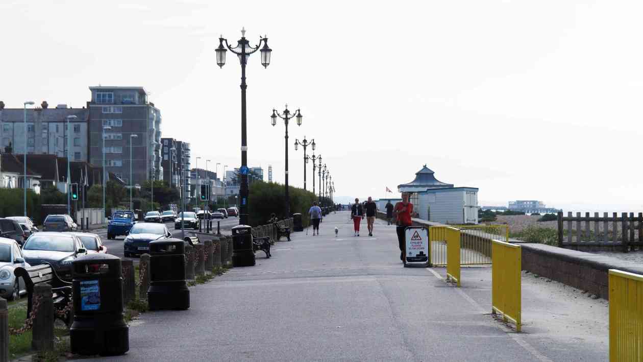 Promenade mit Gehweg, Laternen und Verkehr, von der Menschen spazieren gehen, am Meer entlang.